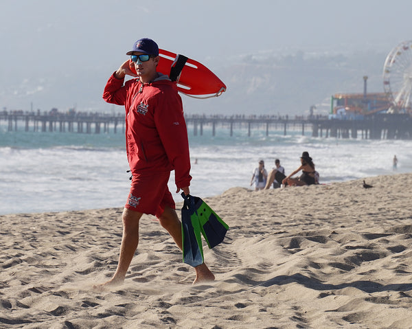 lifeguard with Nöz signature sunscreen on his nose as he carries his raft towards the ocean.